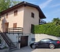 Two-story house with beige exterior, wooden shutters, balcony, garage, and parked car.