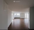 Empty room with wooden flooring, white walls, and large windows allowing natural light. No furniture or equipment present.