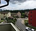 Balcony view overlooking a quiet residential street with houses, greenery, and parked cars.