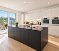 Modern kitchen with white cabinets, dark island, stainless steel appliances, and large windows overlooking a scenic view.