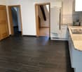 Empty kitchen with dark tiled floor, white cabinets, and a refrigerator. No furniture or appliances are present.