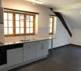 Modern kitchen with wooden-framed windows, white cabinets, dark tiled floor, and stainless steel sink.