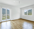 Empty room with wooden flooring, white walls, large windows, and a sliding glass door leading to a balcony with a scenic mountain view.