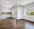 Empty room with white walls, wooden flooring, white cabinets, and large windows offering a scenic view.