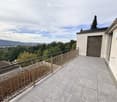Balcony with tiled floor, metal railing, and scenic view of trees and distant landscape.