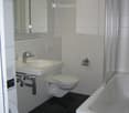 Modern bathroom with white tiles, black floor, sink, toilet, bathtub, and mirror.