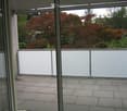 Balcony with tiled floor, white sliding glass doors, and a view of trees and a house in the background.