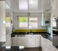 Modern kitchen with white cabinets, black countertops, stainless steel appliances, and a window view of greenery.