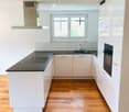 Modern kitchen with white cabinets, black countertops, wooden flooring, and a large window.