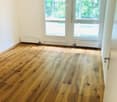 Empty room with wooden flooring, white walls, large windows, and radiators.