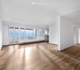 Bright, unfurnished room with wooden flooring, large windows offering a city view, and white walls.