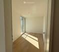 Empty hallway with wooden flooring, white walls, and a glass door leading to a balcony.