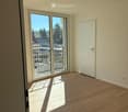 Empty room with wooden flooring, white walls, and large sliding glass doors leading to a balcony or outdoor area.