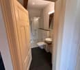 Modern bathroom with dark tiled floor, white walls, toilet, sink, mirror, and glass-enclosed shower area.