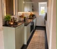 Modern kitchen with light green cabinets, black countertops, and stainless steel appliances. Features a sink, oven, coffee maker, and various kitchen items on the counter.