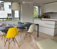 Modern open-plan living and dining area with a sleek black dining table, colorful chairs, white kitchen cabinets, and a pendant light hanging from the ceiling.