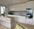 Modern kitchen with white cabinets, a wooden countertop, a sink, and a small seating area visible through a large window.