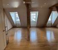 Empty attic room with wooden floors, exposed wooden beams, and skylight windows offering a view of the roof.