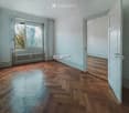 Empty room with wooden flooring, light blue walls, large window with radiator below, and two open doors leading to adjacent spaces.