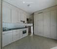 Empty kitchen with white cabinets, a sink, and an oven. The space is clean and unfurnished.