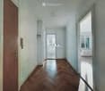 Empty hallway with wooden flooring, white walls, and a closed door on the left. A small window is visible on the right wall.
