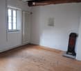 Empty room with wooden flooring, white walls, exposed wooden beams on the ceiling, a window with shutters, a radiator, and a small decorative item in the corner.