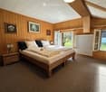 Cozy bedroom with wooden walls, two single beds, nightstand, lamp, radiator, and picture frames on the wall.