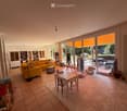 Bright living room with large glass doors leading to a patio, yellow sofa, coffee table, small dining table with chairs, bookshelf, and various toys.