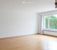 Empty room with wooden flooring, white walls, large window with white frame and curtain, radiator below window, and a chandelier hanging from the ceiling.