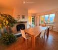 Dining room with a wooden dining table, white chairs, a brick fireplace, and large windows offering a scenic view.