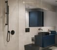 Modern bathroom with glass shower enclosure, black shower head, blue cabinets, black toilet, black sink, and a mirror.