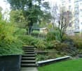 A landscaped garden with steps, greenery, and a small play structure in the background.