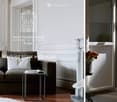 A stylish living room with a grey sofa, small table, bookshelf, and decorative vase with flowers. Large windows and elegant wall moldings.