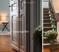 Entrance hallway with a wooden door, patterned tile floor, small table, and lamp. Staircase with metal railing and potted plant on landing.