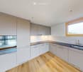 Modern kitchen with white cabinets, wooden flooring, and stainless steel appliances including an oven and sink.