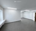 Empty room with white walls, grey carpeted floor, and built-in white cabinetry. Features a window with blinds and a door leading to another room.