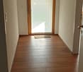 Empty hallway with wooden flooring, light-colored walls, and a small rug near a glass door leading outside.