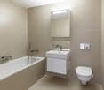 Modern bathroom with beige tiled walls and floor, featuring a bathtub, a sink with a mirror, and a toilet.