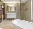 Modern bathroom with a freestanding bathtub, a white sink with a built-in cabinet, and a large mirror above it. The space features light beige tiles and a glass-enclosed shower area.