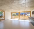 Open-plan space with large sliding glass doors leading to a balcony, modern kitchen cabinets, and a high, exposed wooden ceiling.