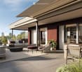 A modern outdoor patio with a sofa, chairs, a coffee table, and a dining table, surrounded by potted plants and a view of greenery.