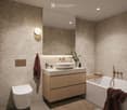 Modern bathroom with a sink, bathtub, toilet, and a large mirror. Features a wooden vanity with drawers, a towel, and decorative items on the counter.