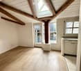 Empty attic space with wooden beams, skylight window, wooden flooring, and white walls. No furniture or equipment present.