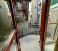 Balcony overlooking a narrow alleyway with metal railing, glass panels, and wooden frame.