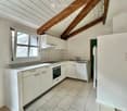 Modern kitchen with white cabinets, stainless steel appliances, and a marble tile floor. Features an exposed wooden ceiling beam and a window with multiple panes.