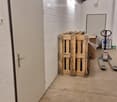 Empty storage area with concrete floor, white brick walls, and a wooden pallet stack. A door is visible on the left, and a forklift is positioned near the back wall.