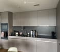 Modern kitchen with grey cabinets, black countertops, stainless steel sink, and various appliances including an oven, coffee maker, and bowl on the counter.