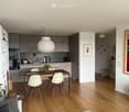 Modern kitchen and dining area with wooden flooring, white cabinets, stainless steel appliances, a round pendant light, and a dining table with chairs.