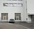 Modern white building with large garage doors and a parked car in front.