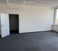 Empty room with grey carpet, white walls, large window, and a closed door.